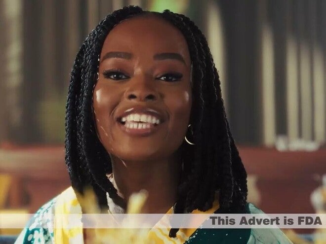Photo of person with braided hair, face blurred, wearing yellow patterned top, indoor blinds